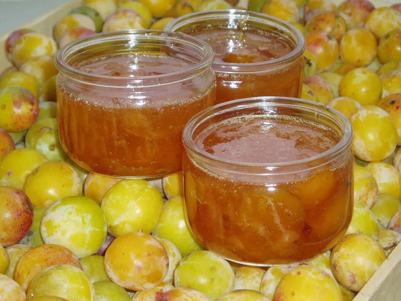 Cocotte en émail ouverte avec une confiture de mirabelles dorée, cuillère en bois et torchon à carreaux à côté