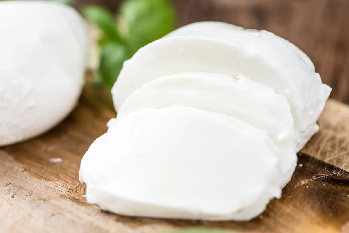 Assiette simple avec tranches de mozzarella fraîche, quelques feuilles de basilic et un rayon de lumière sur un plan de travail en bois